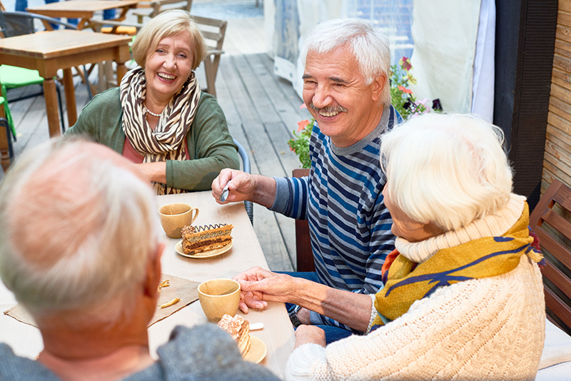 Older adults having coffee and cake on an outdoor deck.